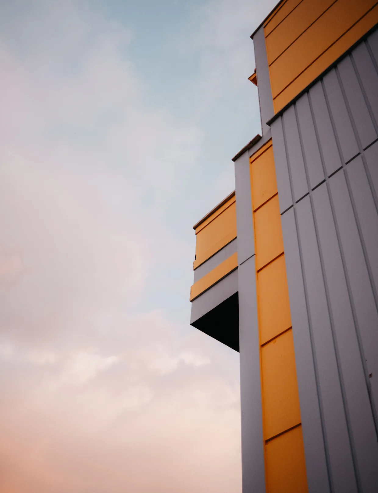 Die Fassade eines Gebäudes aus orangen und grauen Sandwichpaneelen vor Abendhimmel.