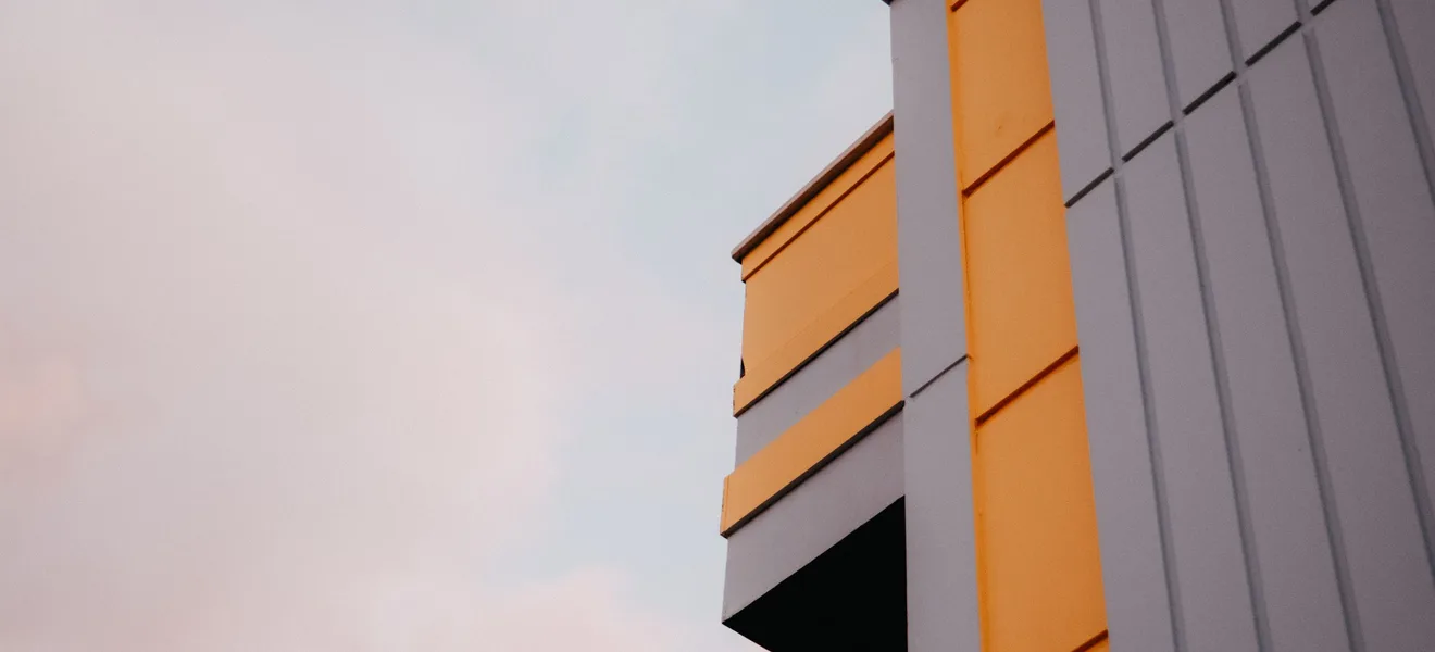 Die Fassade eines Gebäudes aus orangen und grauen Sandwichpaneelen vor Abendhimmel.