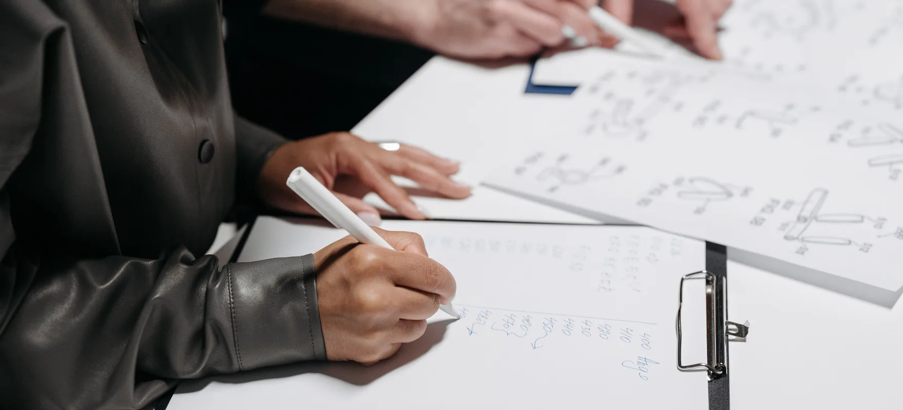 Zwei Personen sitzen an einem Tisch, schreiben eine Liste auf Papier und zeichnen daneben eine Skizze.