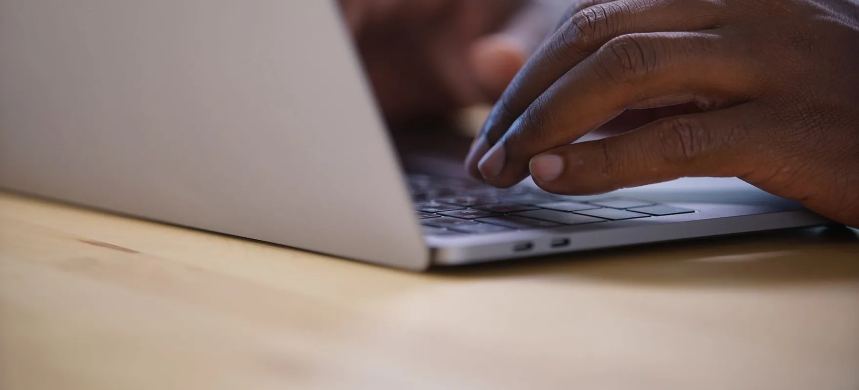 Zwei Hände tippen auf der Tastatur eines aufgeklappten Laptops, daneben liegt ein Notizblock.