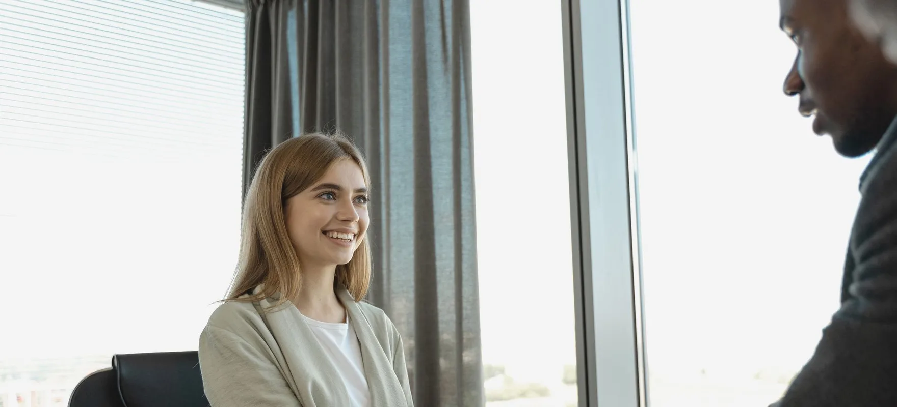 Ein Gespräch am Fenster: eine Frau sitzt lächelnd an einem Tisch, ihr gegenüber ein Kollege.