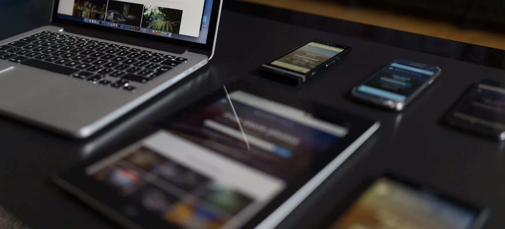Ein Notebook, ein Tablet und zwei Mobiltelefone auf einem dunklen Tisch zeigen dieselbe Website.