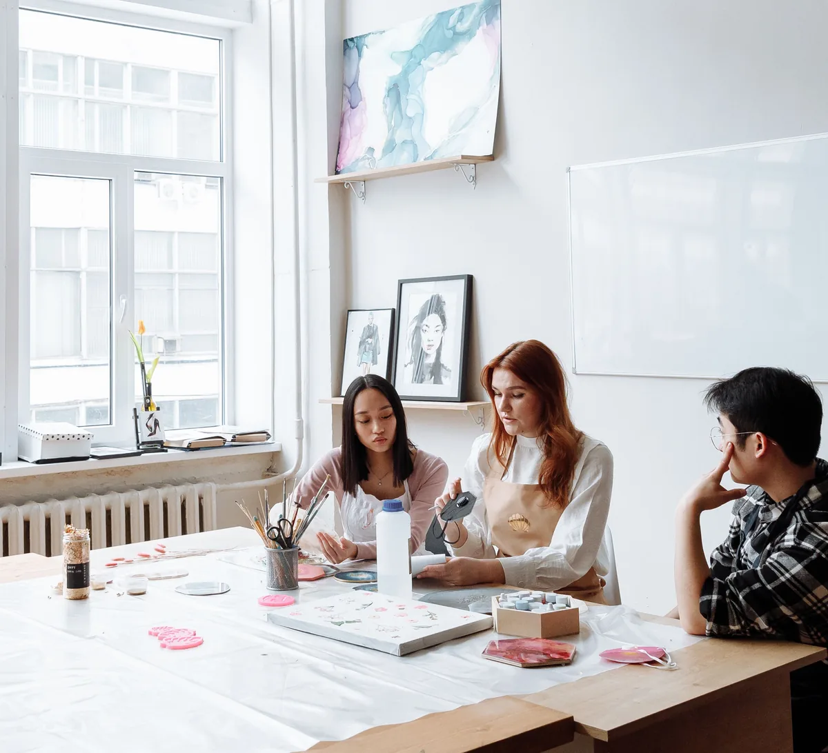 Drei Menschen sitzen an einem langen Tisch in einem hellen Studio und arbeiten.