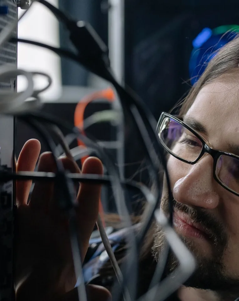 Ein Techniker steht hinter einem Bündel Netzwerkkabel und prüft eine Verbindung.