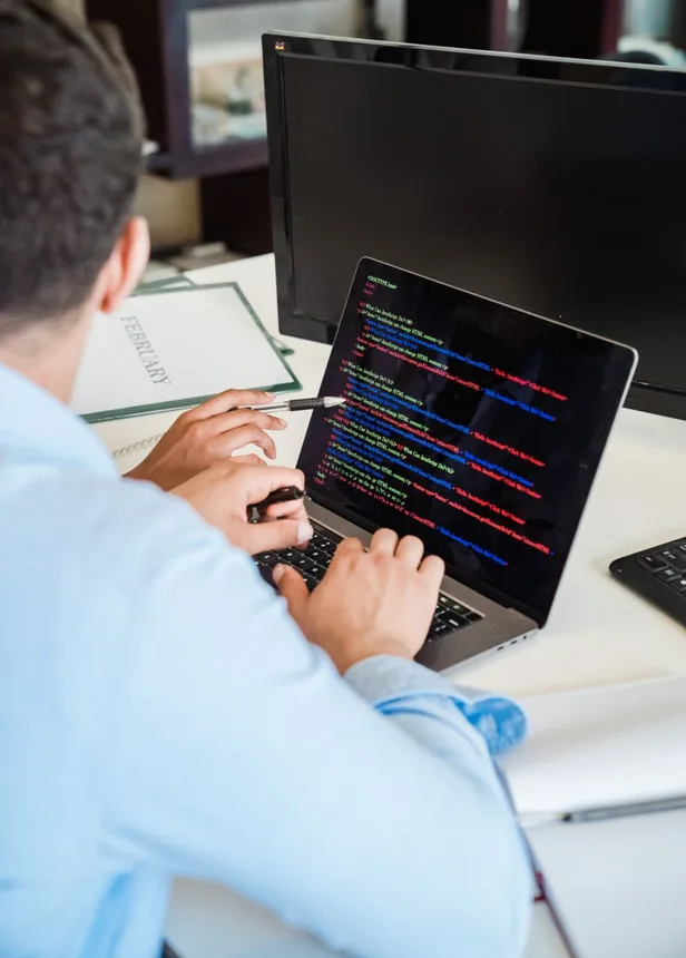 Eine Person arbeitet an einem Notebook, auf dem Bildschirm steht Programmcode.