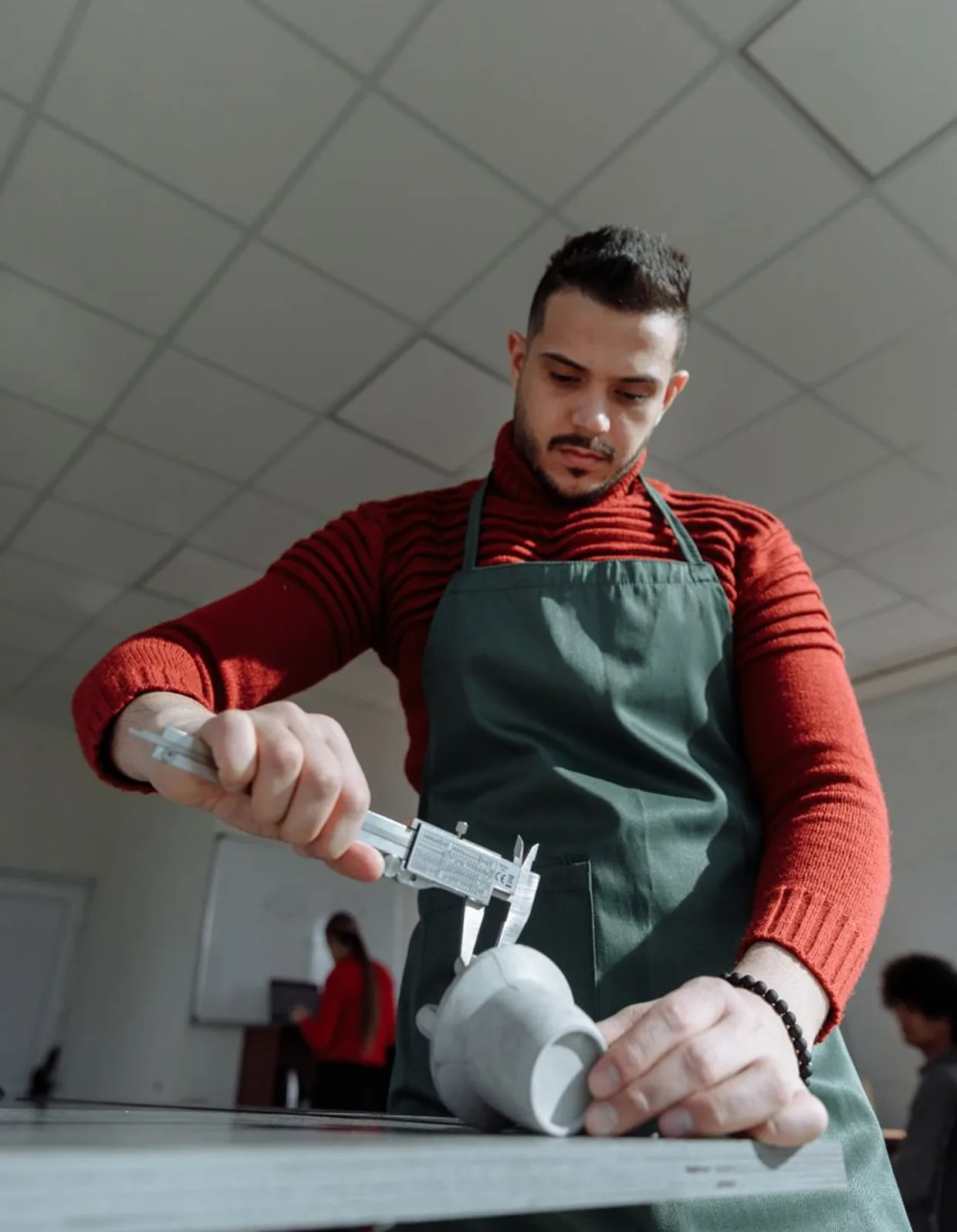 Ein Mann in Arbeitsschuerze steht in seiner Werkstatt und haelt ein Werkstueck in der Hand.