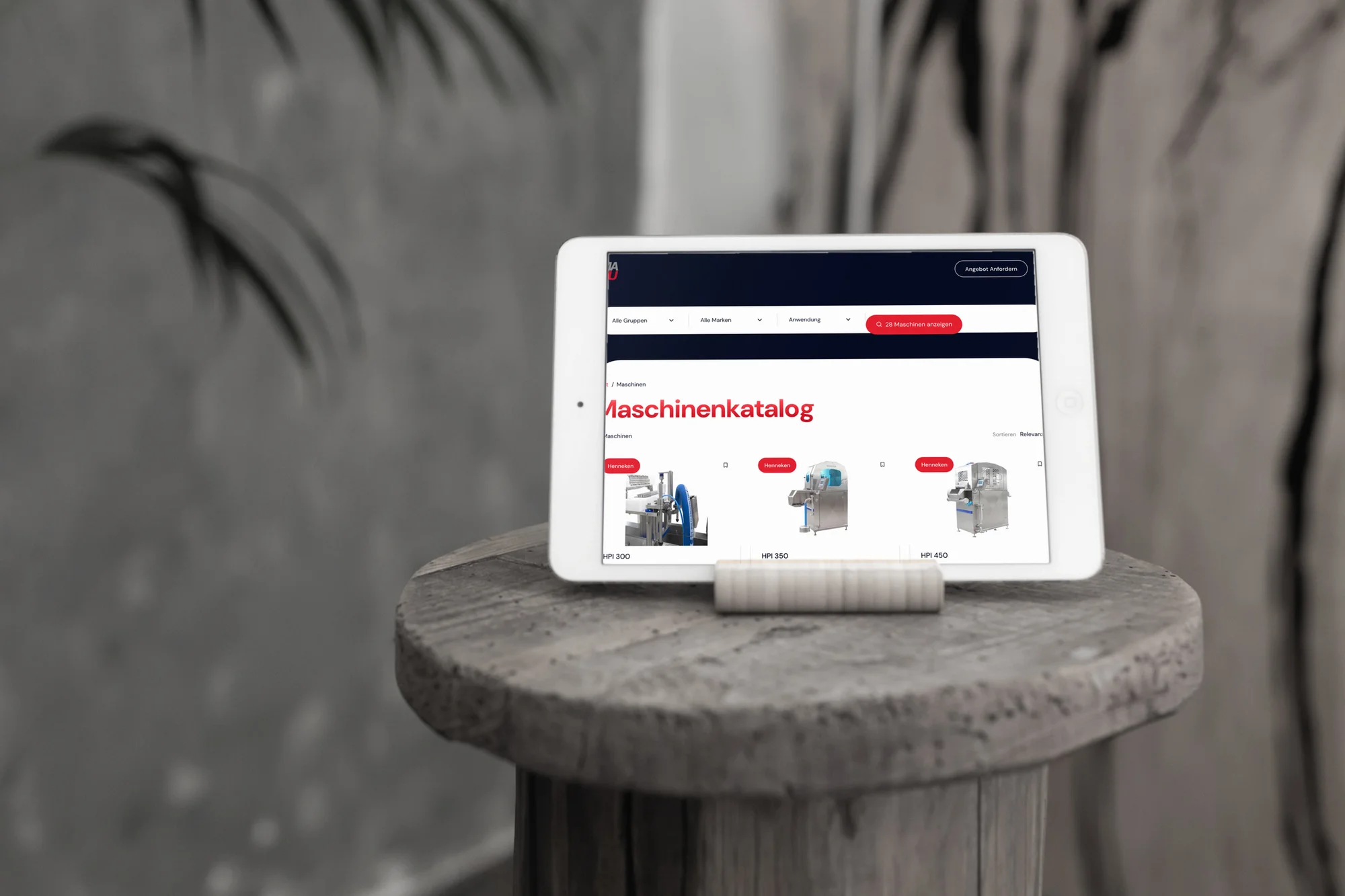 Der Maschinenkatalog von MAKU Meat Tec auf einem iPad, das auf einem runden Holzhocker steht.