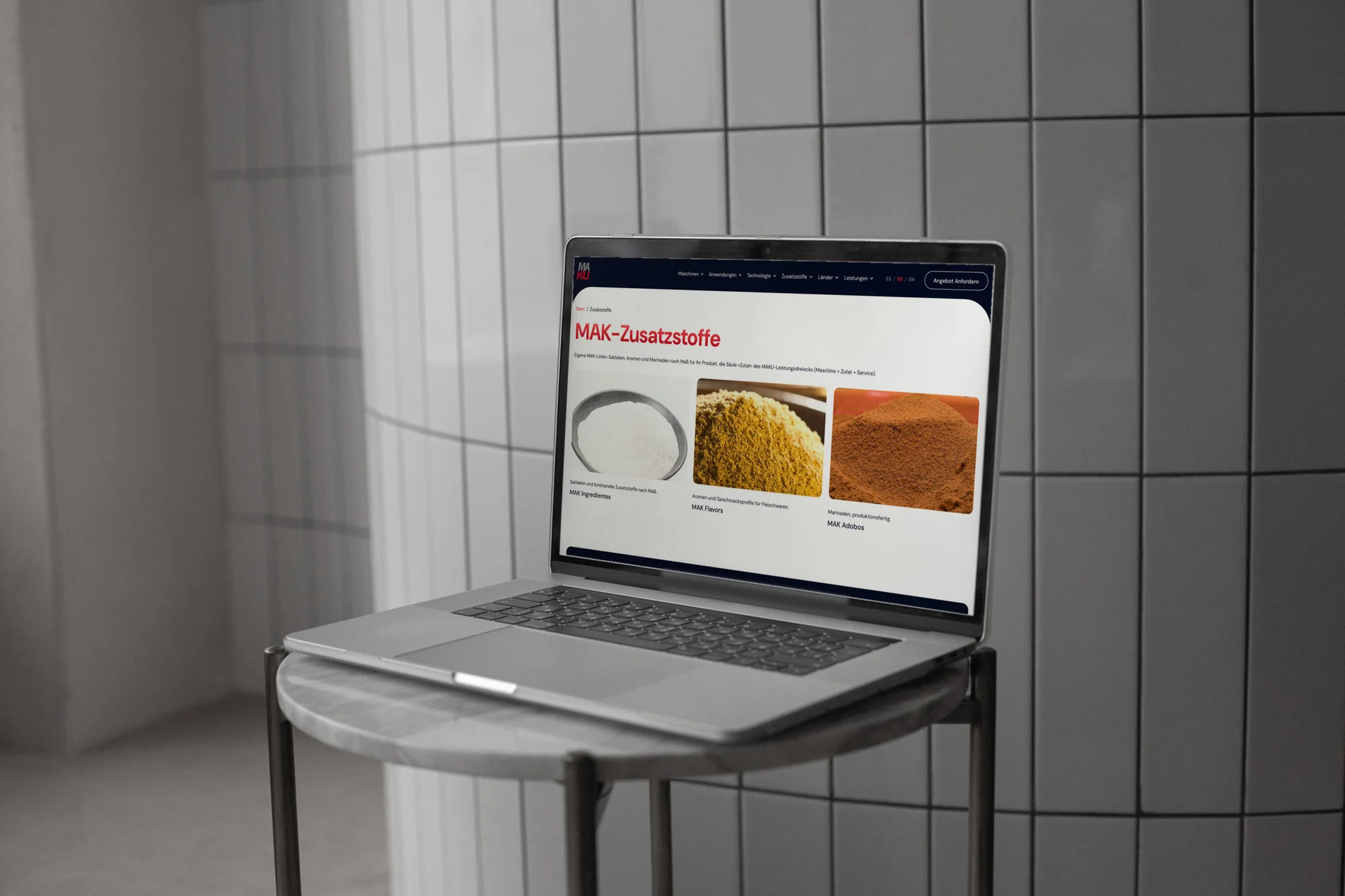 Die Seite MAK-Zusatzstoffe von MAKU Meat Tec auf einem MacBook, das auf einem Beistelltisch vor einer gefliesten Wand steht.