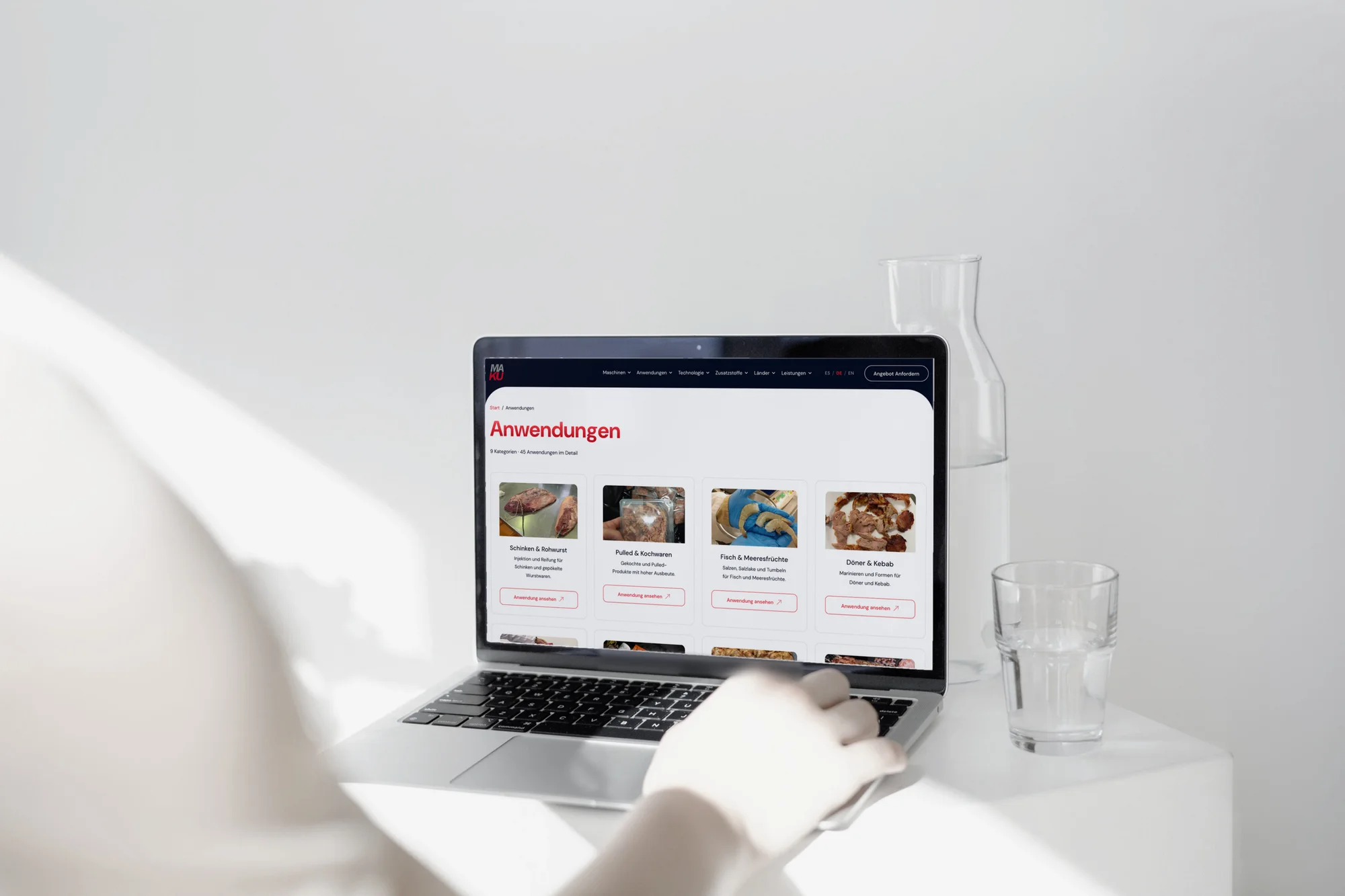 Die Anwendungsseite von MAKU Meat Tec auf einem MacBook, daneben eine Karaffe und ein Glas auf weißer Fläche.