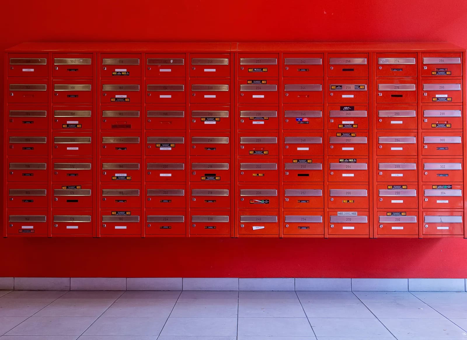 Eine Wand aus roten Briefkästen mit nummerierten Klappen vor einer roten Wand.