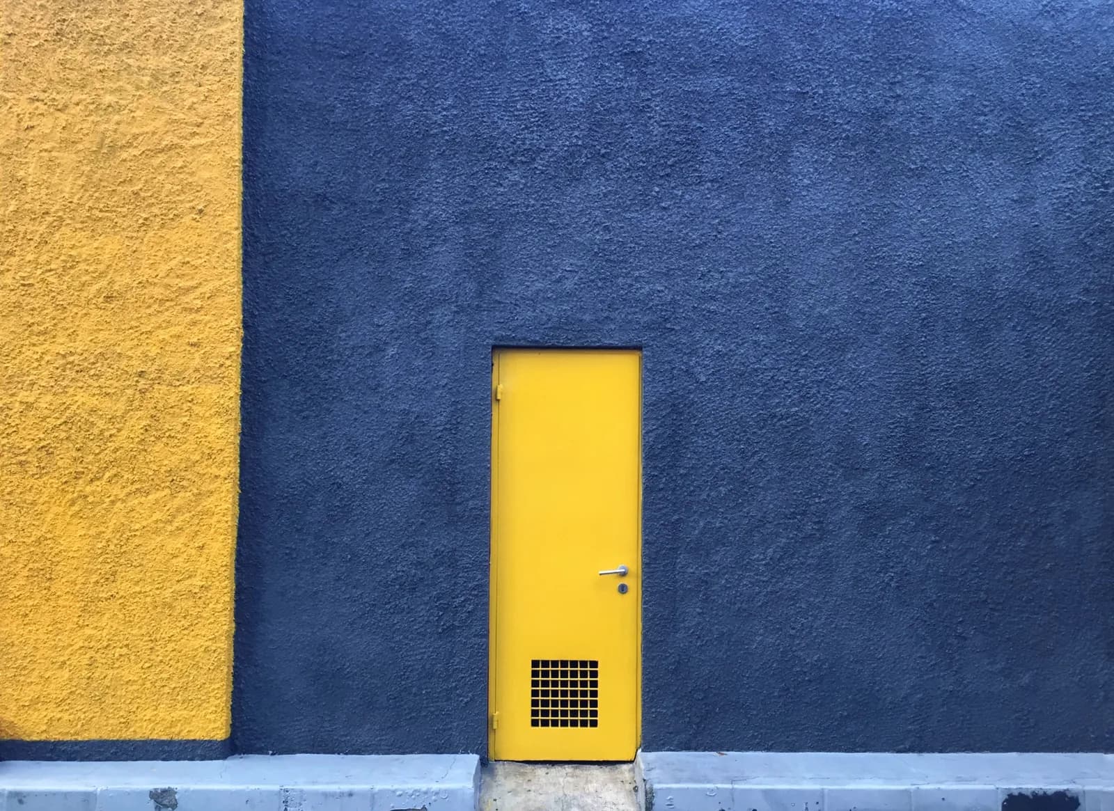 Eine geschlossene gelbe Stahltür in einer tiefblauen Hauswand.